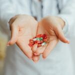 Krwawienia w środku cyklu a antykoncepcja: kiedy to skutek uboczny, a kiedy znak problemu Dłonie kobiety trzymające kolorowe tabletki antykoncepcyjne