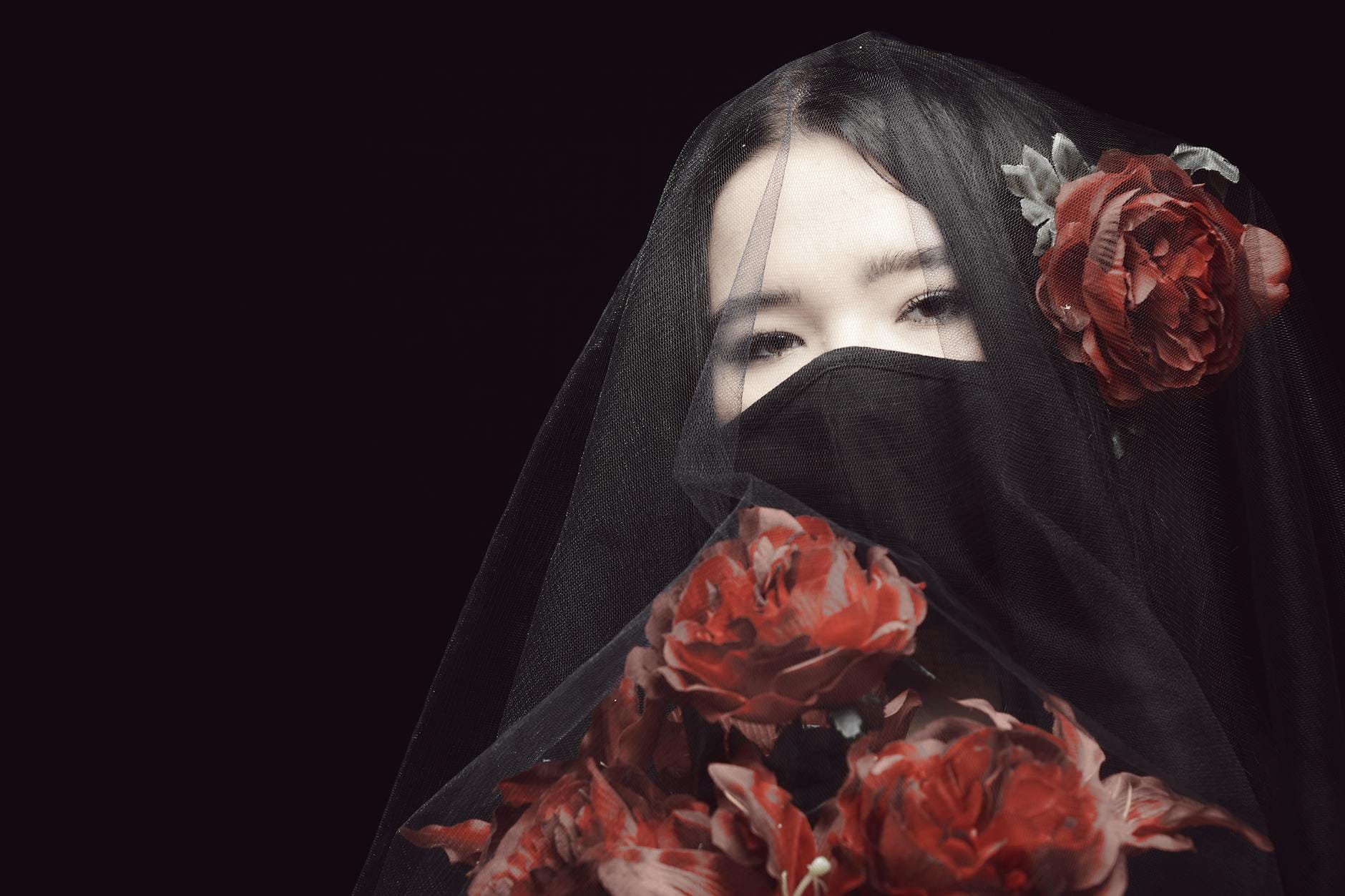 Kobieta w czarnej woalce z czerwonymi różami, zamyślona i poruszona