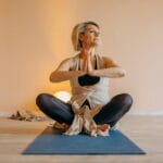 Menopauza a miesiączka: kiedy cykl naprawdę się kończy? Kobieta w średnim wieku medytuje w domu, siedząc w pozycji lotosu