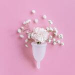 Miesiączka dwa razy w miesiącu: możliwe przyczyny i co sprawdzić Różowy kubeczek menstruacyjny z kwiatami na pastelowym tle