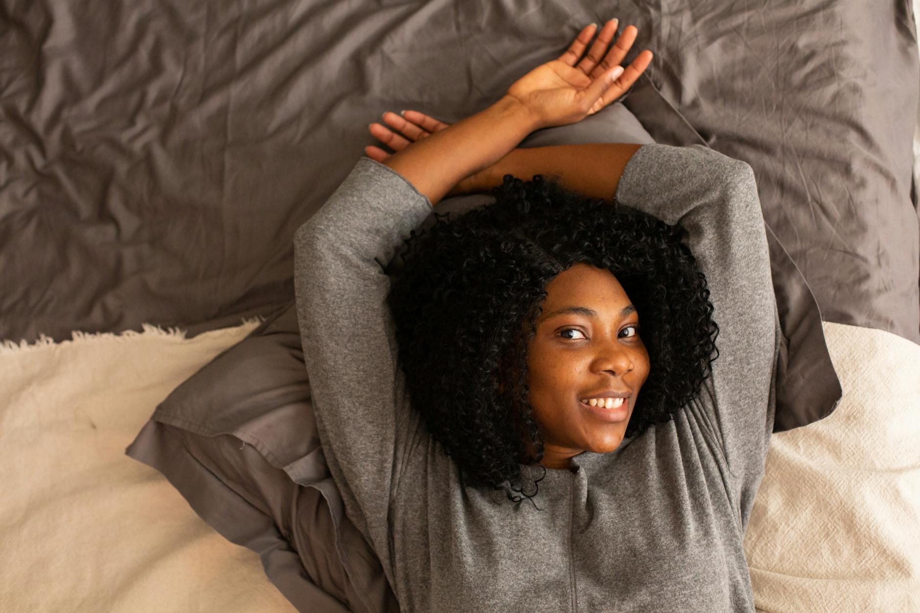 Uśmiechnięta kobieta leży wygodnie na łóżku z rękami za głową