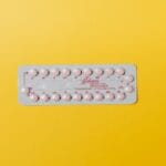 Blister różowych tabletek antykoncepcyjnych na żółtym tle
