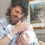 Mama tuląca noworodka na szpitalnym łóżku po porodzie